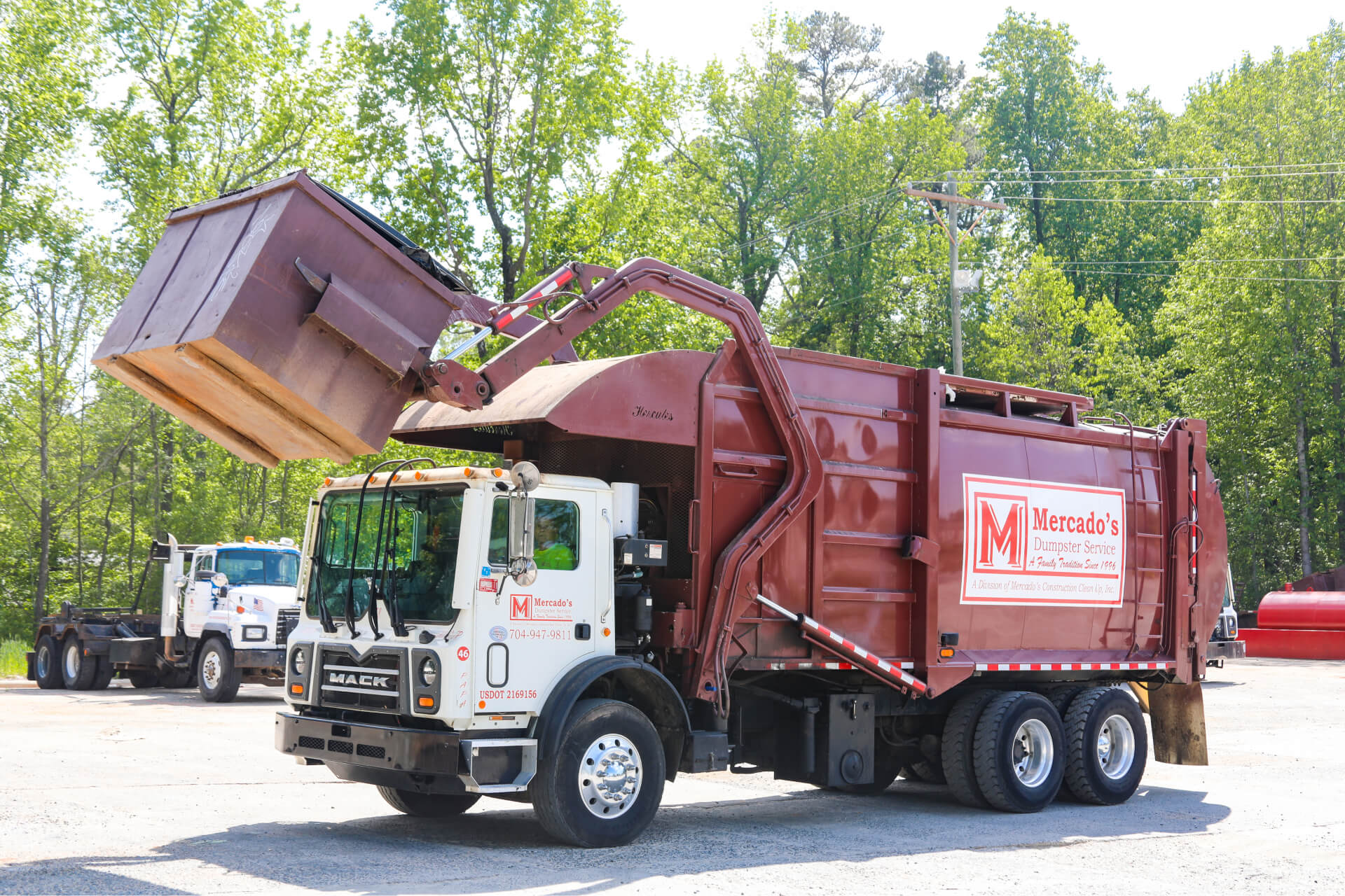 A front load dumpster truck lifting a dumpster labeled with Mercados Dumpsters
